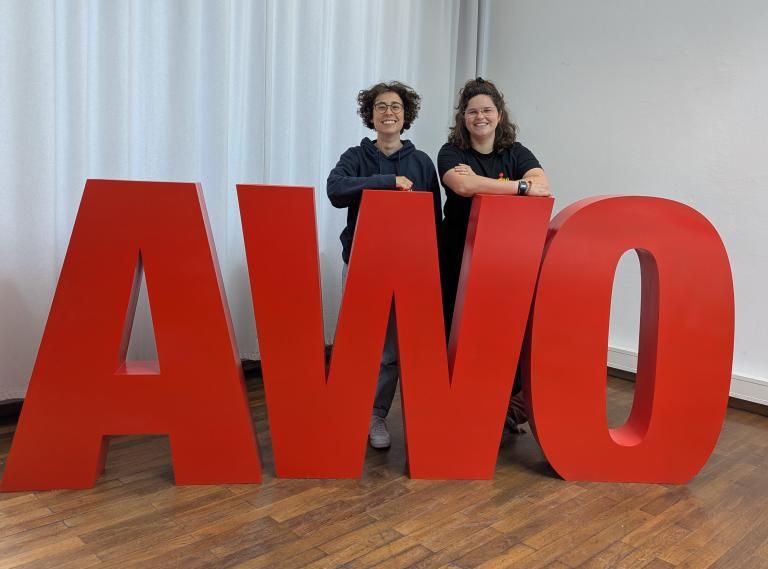 Anna (links) und Roxana (rechts) stehen hinter einem großen AWO-Aufsteller in roten Buchstaben