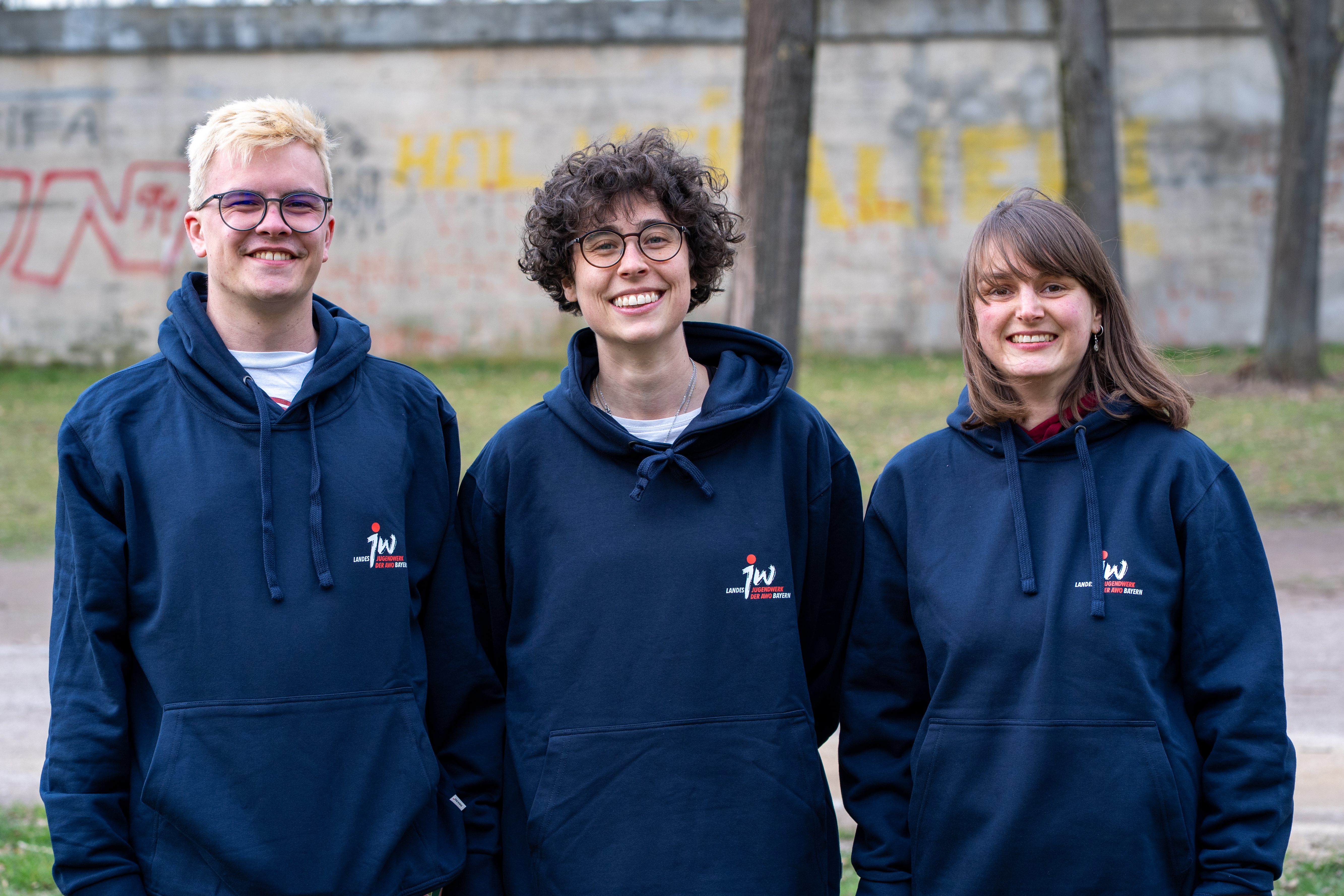 Dreie neue Vorstandsmitglieder werden draußen fotographiert und tragen Pullis vom Landesjugendwerk.